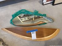 Organic-shaped frameless mirror partially wrapped in green bubble wrap alongside curved wood shelf.