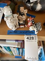 Four clay figurines grouped on wood shelf: white bear with cubs, female figure, fox family, zebra