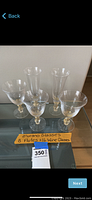 Three flutes and three wine glasses on glass table with handwritten note and lot tag visible