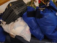Photo showing multiple blue fabric storage bags and a clear plastic bag filled with women's clothing, with a patterned black carry on bag on top.