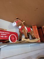 Side and front view of the plush rocking horse mounted on wooden rockers, next to the wooden firefighter truck and doll box on shelf.