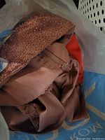 Brown satin gown with bead embellishments shown inside a plastic bag