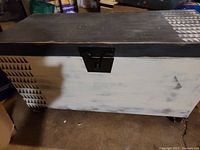 Front and top view of the wooden storage chest showing the black and white paint with geometric triangle patterns and the metal latch on the front.