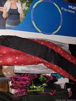 Weighted fitness hoop box with woman in workout attire on the front, red and black back support belt, and part of pink and green gloves visible.