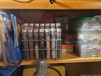 Tubes filled with beads and plastic storage containers on wooden shelf.