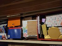 Wide view of drawer containing journals, calendar pads, photo paper packs, and various stationery and office supplies in boxes and envelope-like holders.