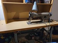 Front-left angle of Juki DDL-555 mounted on a wooden table with a metal base and attached light above sewing area