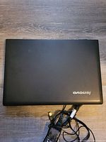 Top view of closed Lenovo laptop with charger beside it on a wood floor.