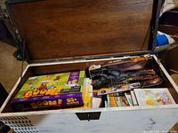 Overview photo of open wooden chest with various boxed and packaged toys including science kit, dinosaur figures, and cartoon character toy sets.