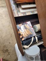 Photo showing open wooden drawer with a drawer organizer containing wooden handles, plastic bag of wood handles, fabric rolled-up item, and bin lid.