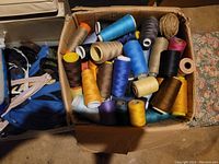 Overview of box containing various spools of thread, zippers and other sewing materials in multiple colors.