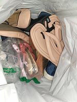 Photo showing multiple pairs of women's shoes inside a white plastic bag, beige padded lining visible on some, mixed colors including black and beige.