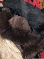 Image showing bundled winter jackets including brown suede with real fur trim, a black fur-lined jacket, and portions of a red jacket in the background.