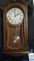 Full front view of the Bulova wall clock showing wooden case, clock face with Roman numerals and pendulum detail.