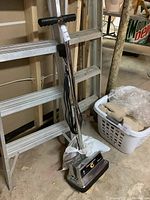 Full view of Koblenz floor cleaning machine upright with chrome handle and black power cord wrapped around it in a garage setting.