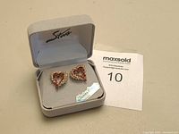 Front view of the heart-shaped 14K gold earrings in a grey padded presentation box with 'Stone' branding.
