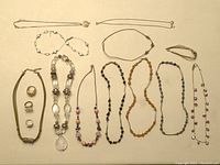 Overhead shot of all jewelry laid out on flat cream background, showing assortment of necklaces, rings, bracelets, earrings and brooch