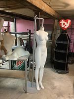Full view of white female headless mannequin on metal stand with adjustable height mechanism in basement setting