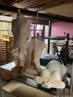 Four mannequin torsos, including visible fabric-covered torsos mounted on wooden stands and white plastic torsos laying on a metal table.