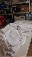 Stacks of folded white cloth napkins and the round embroidered white tablecloth on display on table in storage area.