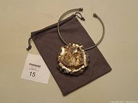 Photo of sterling silver choker with large detailed 3D flower pendant and microfiber pouch on beige background.