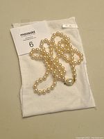 Double strand faux pearl necklace coiled on white cotton storage bag with satin ribbon.