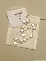 Pearl necklace with sterling silver chain laid on top of a white cotton bag, showing the 20 flat pearl coins.