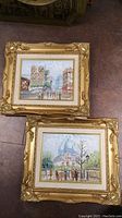 Pair of two ornately framed original acrylic street scene paintings on canvas, showing cityscapes with people and buildings, gold ornate frames.