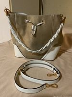 Front view of the Michael Kors handbag showing beige textured body with white leather accents, twisted white leather handle, and flat shoulder strap laid in front.