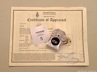 Certificate of Appraisal laid flat with the ring in its acrylic presentation box on top