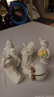 Four Snowbabies figurines and one bell ornament displayed on a table, showing various poses and details