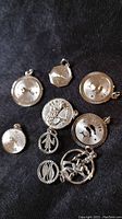 Front view of nine sterling silver charms showing various astrological and zodiac designs including Gemini and Pisces symbols with textured borders.