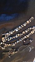 Overview of necklaces and bracelet on black fabric showcasing pearl beads and the angel pendant figure with its chain.