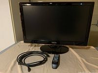 Samsung flat panel TV on stand, remote control in front, and one HDMI cord coiled on left side.