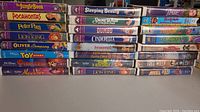 View of 20 VHS movies stacked in two columns showing titles and spine artwork including The Jungle Book, Pocahontas, Peter Pan, The Lion King, Oliver & Company, Toy Story, Pinocchio, Aladdin, Sleeping Beauty, Snow White and the Seven Dwarfs and more.