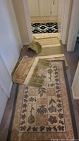 Overview photo showing multiple rugs, a toilet seat cover, and smaller bathroom rugs in neutral and floral patterns.