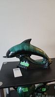 Side view of ceramic dolphin sculpture showing curved body and color gradient from black near the nose to green on the fin and tail.