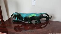 Side view of the Blue Mountain Pottery panther figurine placed on a wooden surface, showing the full body crouching pose with turquoise and dark green glaze.