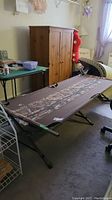 Full view of camping cot setup indoors, showing metal frame, camo fabric surface and surrounding items.