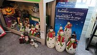 Wide shot of multiple Christmas and Halloween figurines on shelves, showing the set of 3 tall LED snowmen and assorted smaller figurines spread around