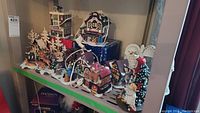 Wide shot showing five ceramic village buildings, deer figurines, carolers and metal archway on shelf