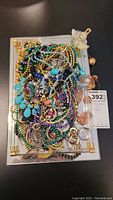 Pile of assorted colorful costume jewellery necklaces on a mirrored tray with gold-tone corners.