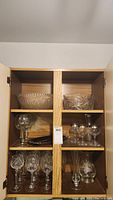 Eight patterned wine glasses, three crystal wine glasses, two vases, and decanter set displayed inside a wooden cabinet