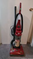 Full front view of the red Dirt Devil Jaguar Bayless upright vacuum cleaner with hose and cord.