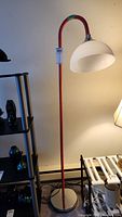 Full view of the floor lamp showing orange extendable arm, round metal base, and white lampshade.