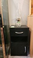 Photo showing full cupboard with drawer and door, and the hurricane lamp placed on top of it.