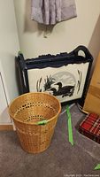 Photo showing the wood magazine rack with loon scene and the wicker waste paper basket placed next to each other on floor.