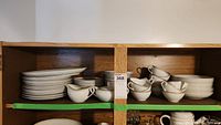 Photo showing multiple stacked plates and cups in a cabinet: salad plates, tea cups, dinner plates, and possibly dessert plates.
