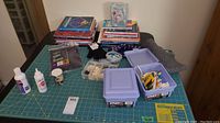 Sewing accessories and books laid out on rotary mat, showing overall lot contents including boxes of buttons, gloves, and instructional books