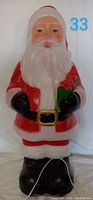 Front view of the 24-inch tall Santa blow mold figure showing the detailed face, red suit, white beard, black gloves and boots, and green gift in hands.
